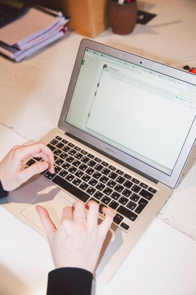 Close-up of hands typing on a laptop at an office desk, suggesting work or online communication.